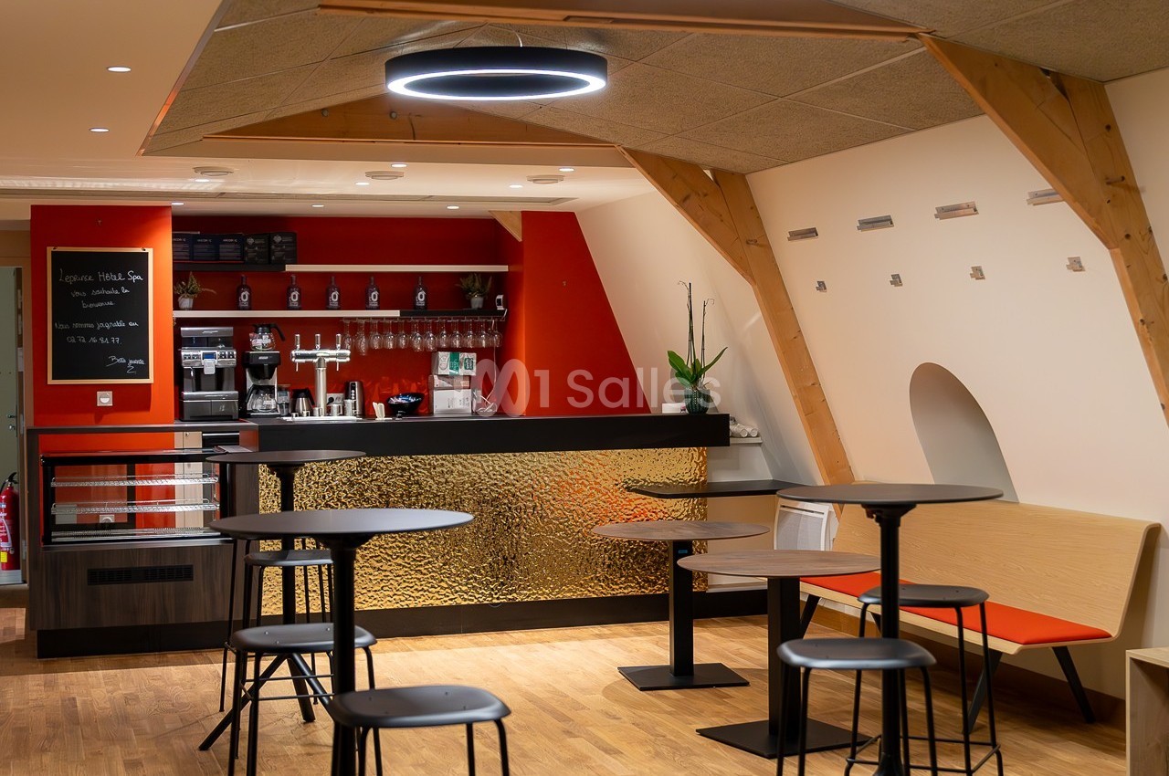 Espace café moderne avec comptoir rouge et noir, tables hautes, chaises et éclairage circulaire suspendu.