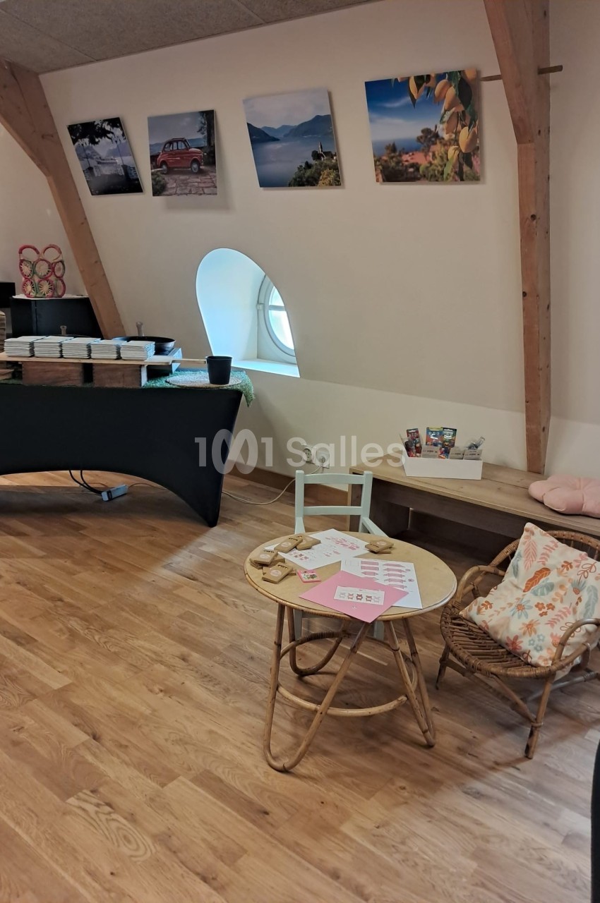 Coin aménagé avec une petite table, des chaises en rotin, des documents et des décorations dans une pièce lumineuse.