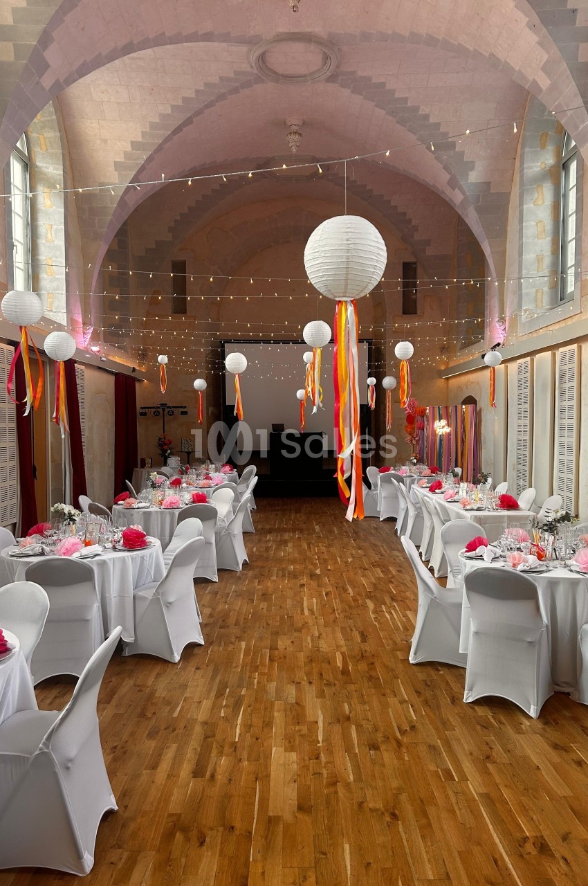Salle de réception décorée avec des tables dressées, des lanternes suspendues et des rubans colorés.