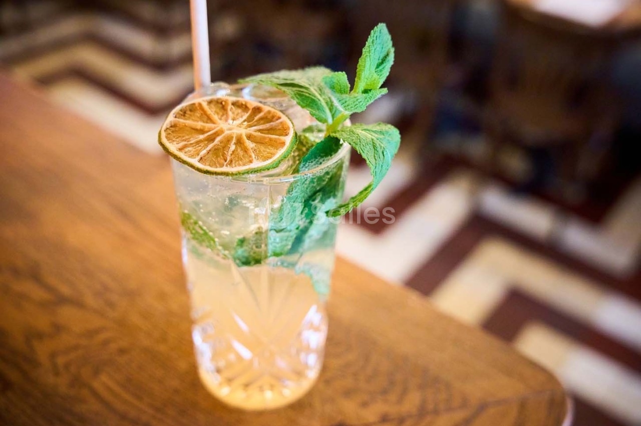 Verre de cocktail garni de menthe fraîche et d'une tranche de citron séché, posé sur une table en bois.
