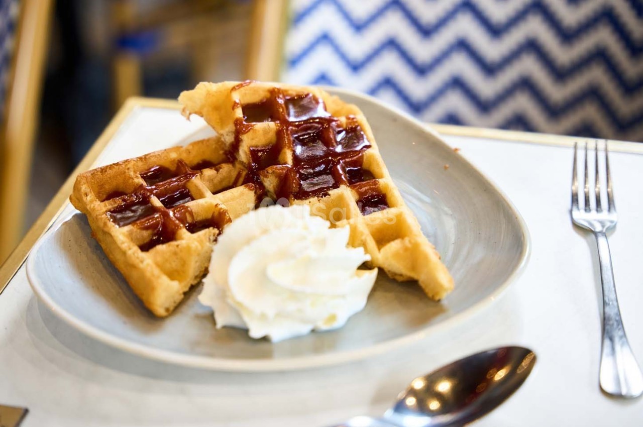 Gaufres dorées avec coulis de fruits rouges et crème chantilly, servies dans une assiette sur une table.