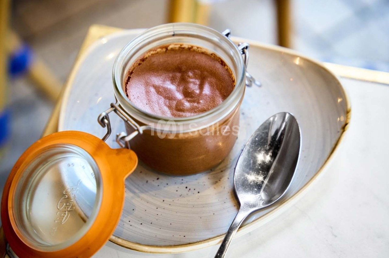 Pot de mousse au chocolat dans un bocal en verre ouvert, posé sur une assiette avec une cuillère en métal.
