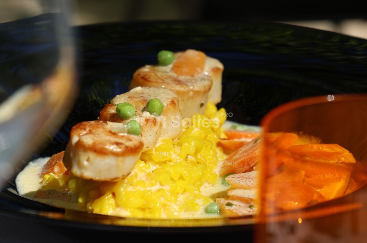 Noix de Saint-Jacques poêlées sur un risotto au safran, accompagnées de carottes et petits pois.