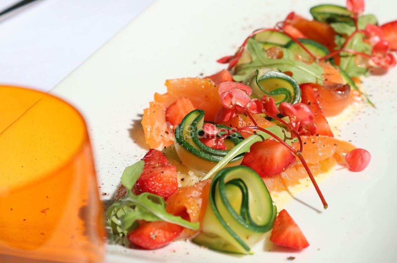Assiette garnie de saumon fumé, courgettes en spirale, fraises fraîches et micro-pousses, présentée sur une table lumineuse.