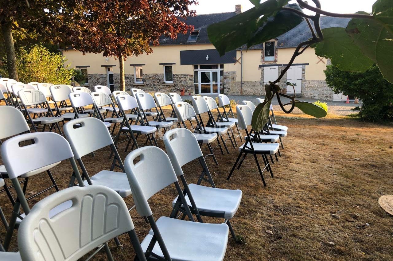 Chaises blanches pliantes disposées en rangées sur une pelouse devant un bâtiment en pierre.