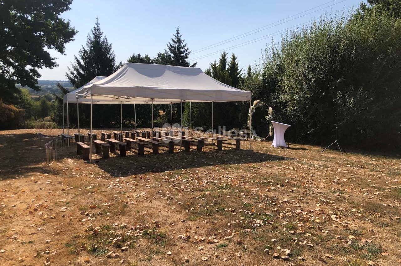 Tente blanche montée dans un espace extérieur avec des bancs en bois disposés pour un événement.