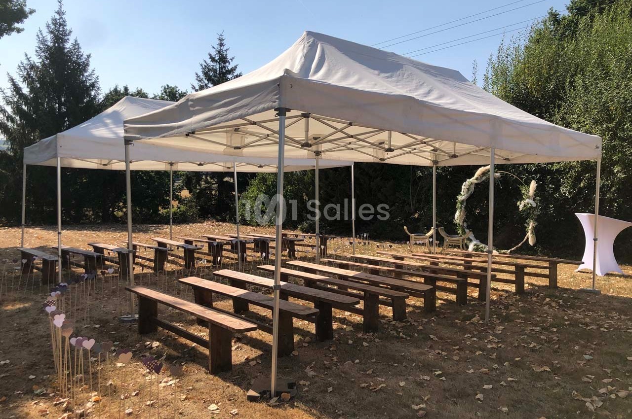 Tentes blanches montées sur une pelouse avec des bancs en bois disposés pour un événement en extérieur.