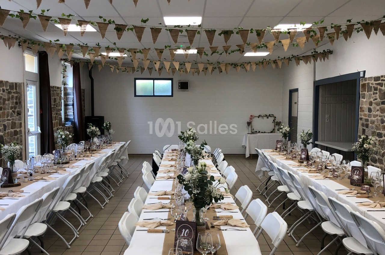 Salle décorée pour un mariage avec longues tables dressées, guirlandes en tissu et compositions florales.