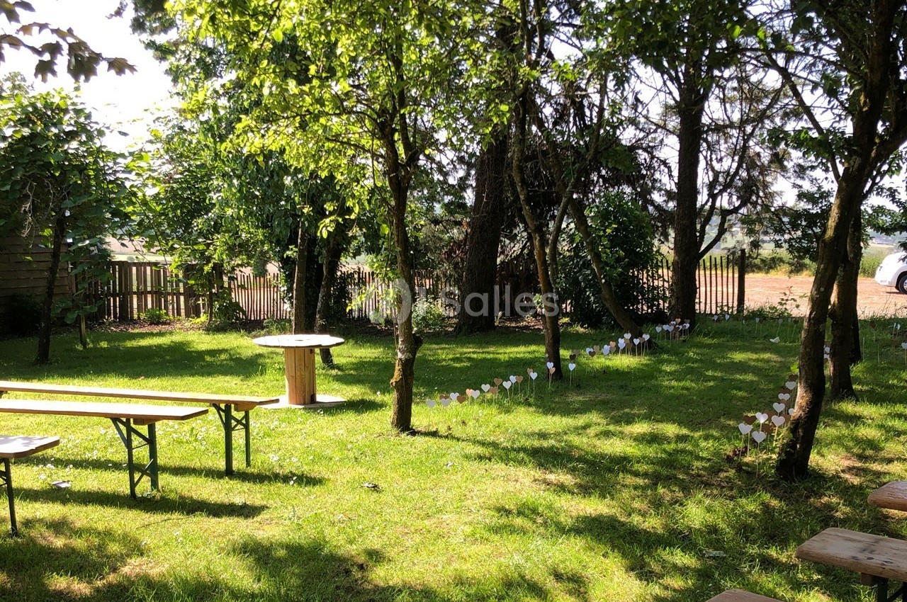Un jardin ombragé avec des arbres, des bancs en bois et des décorations blanches plantées dans l'herbe.
