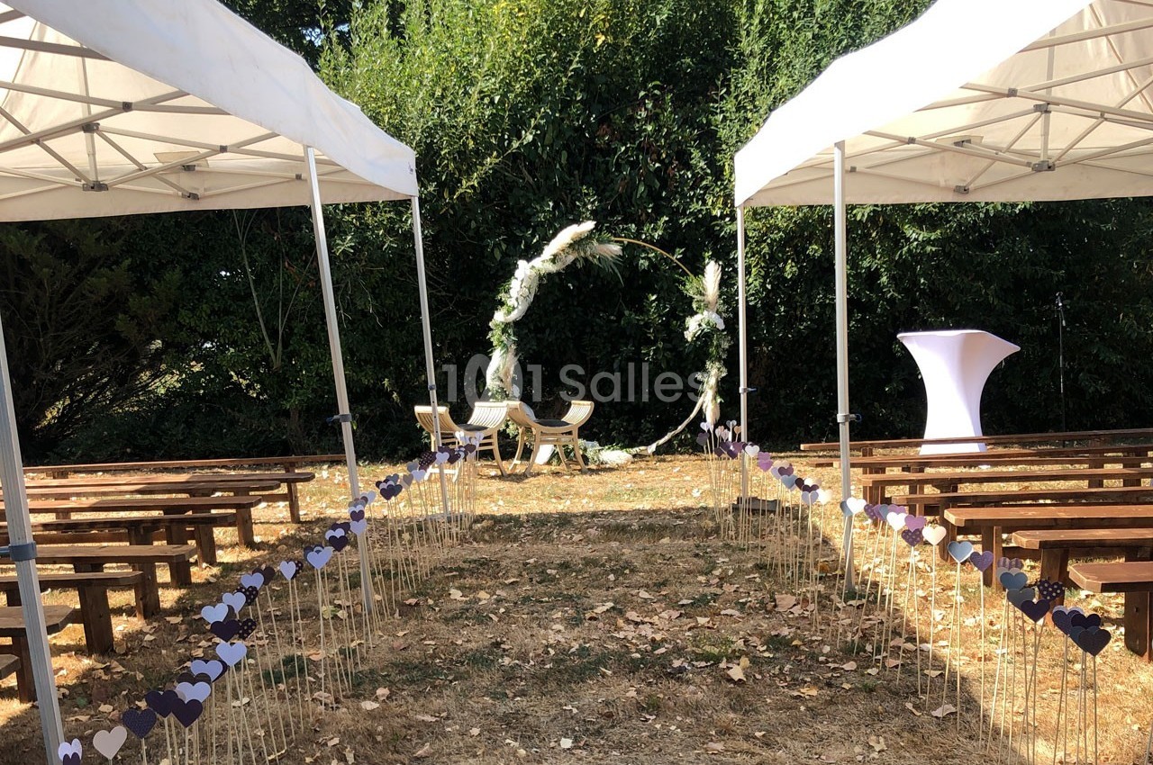 Allée décorée de cœurs menant à une arche florale pour une cérémonie en plein air sous des tonnelles blanches.