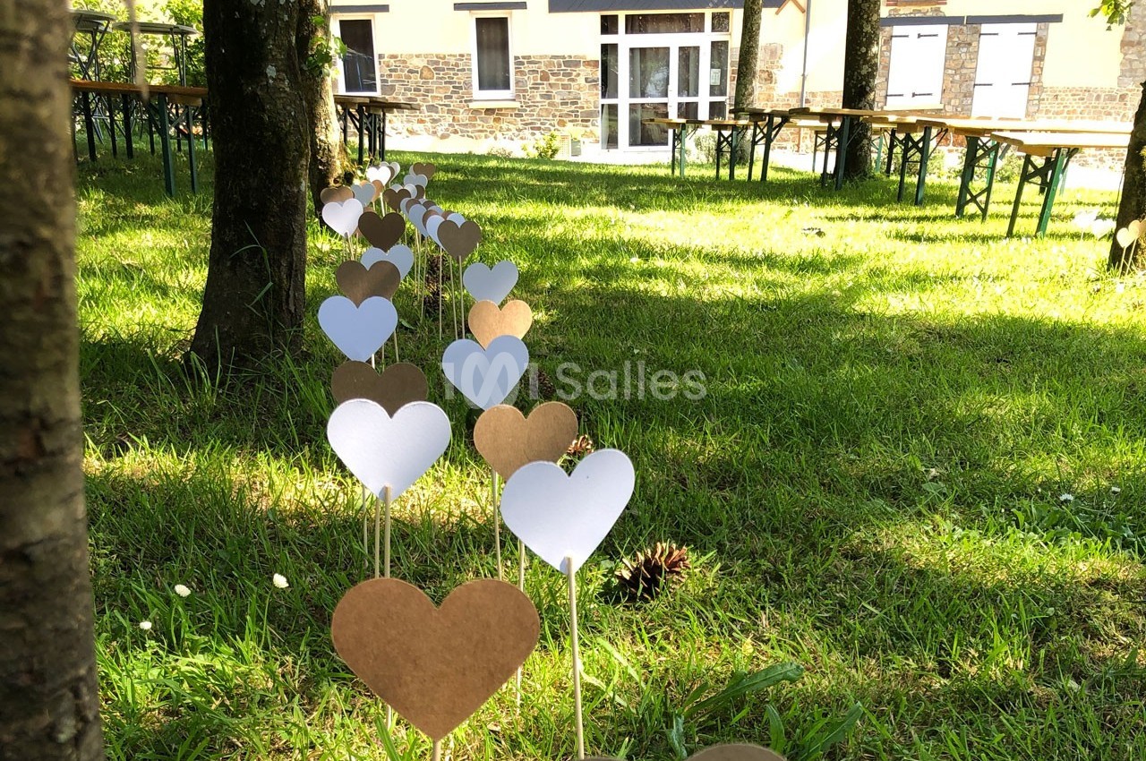 Cœurs en papier blanc et marron plantés sur des tiges dans une pelouse, avec des tables et un bâtiment en arrière-plan.