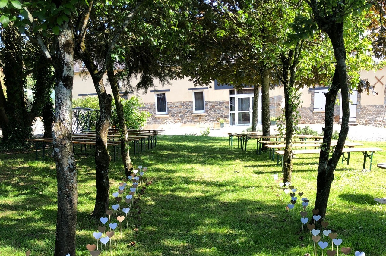 Allée décorée de cœurs en papier menant à des bancs en bois sous des arbres dans un jardin ensoleillé.