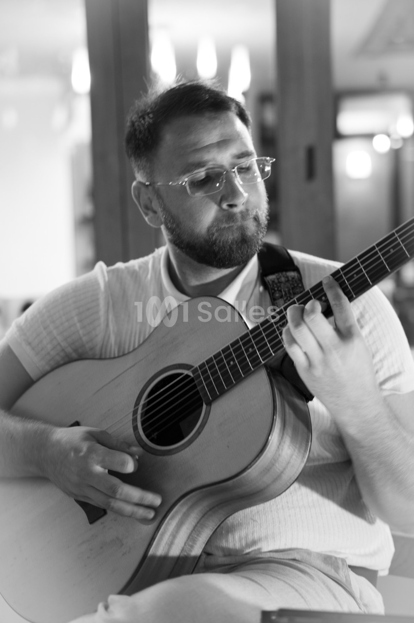 Un homme joue de la guitare acoustique dans un intérieur éclairé, capturé en noir et blanc.