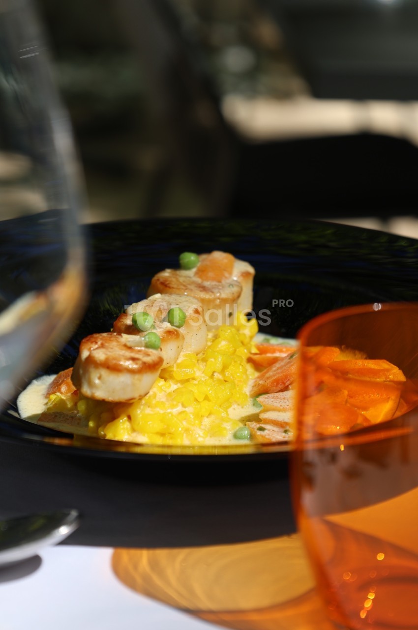 Assiette de risotto au safran, noix de Saint-Jacques poêlées et petits pois, servie avec des légumes en accompagnement.