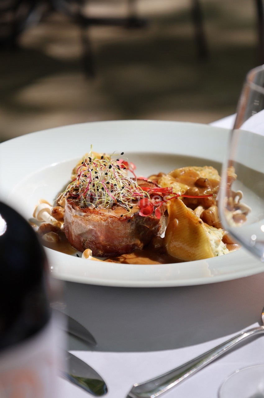 Assiette gastronomique avec viande en sauce, légumes, germes décoratifs et verre de vin en arrière-plan flou.