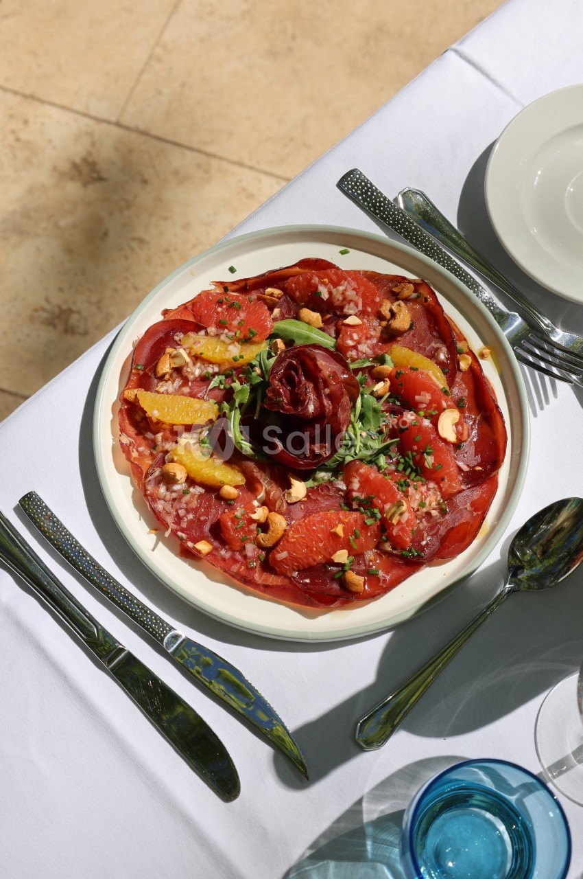 Assiette de carpaccio de bœuf garnie d'agrumes, noix de cajou et herbes fraîches, servie sur une table dressée.