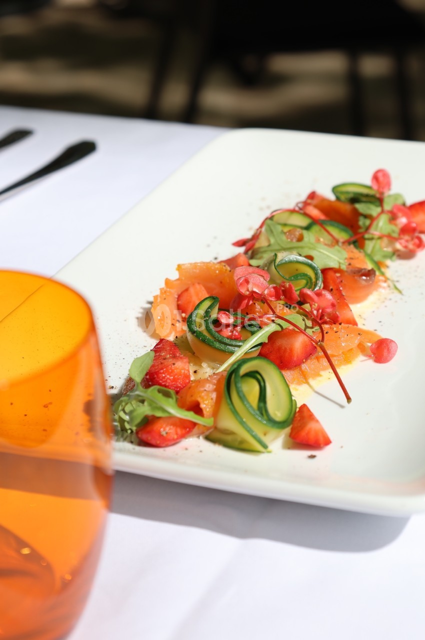 Assiette de saumon fumé garnie de légumes frais, fraises et herbes, présentée sur une table dressée.