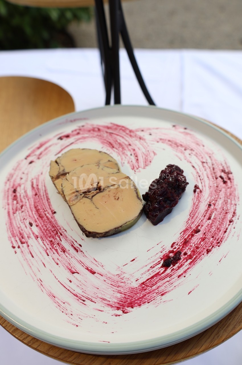 Tranche de foie gras accompagnée d'une confiture de fruits rouges, présentée sur une assiette décorée de coulis.