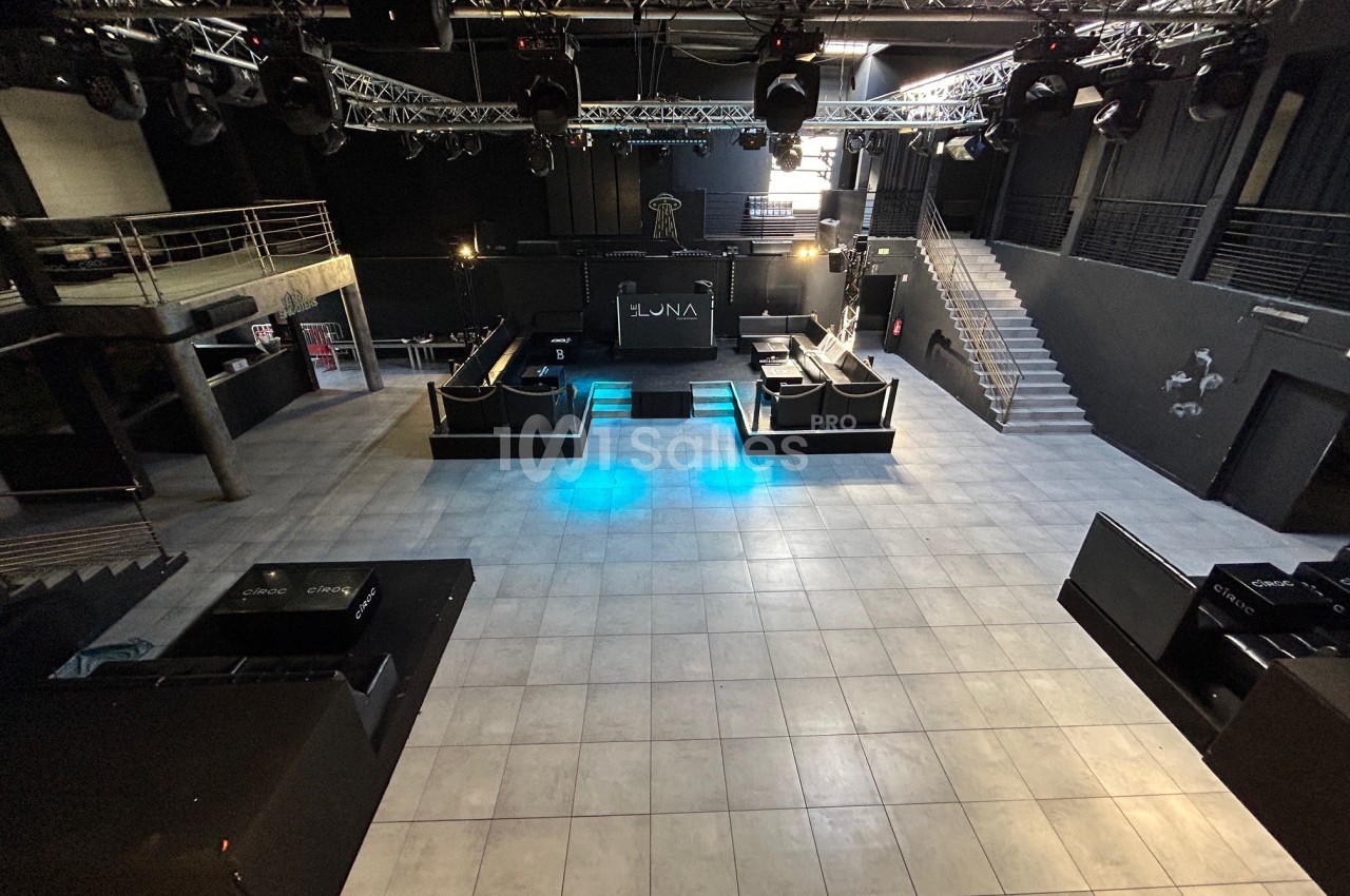 Salle de concert vide avec scène centrale, éclairages suspendus et escaliers menant à une mezzanine.