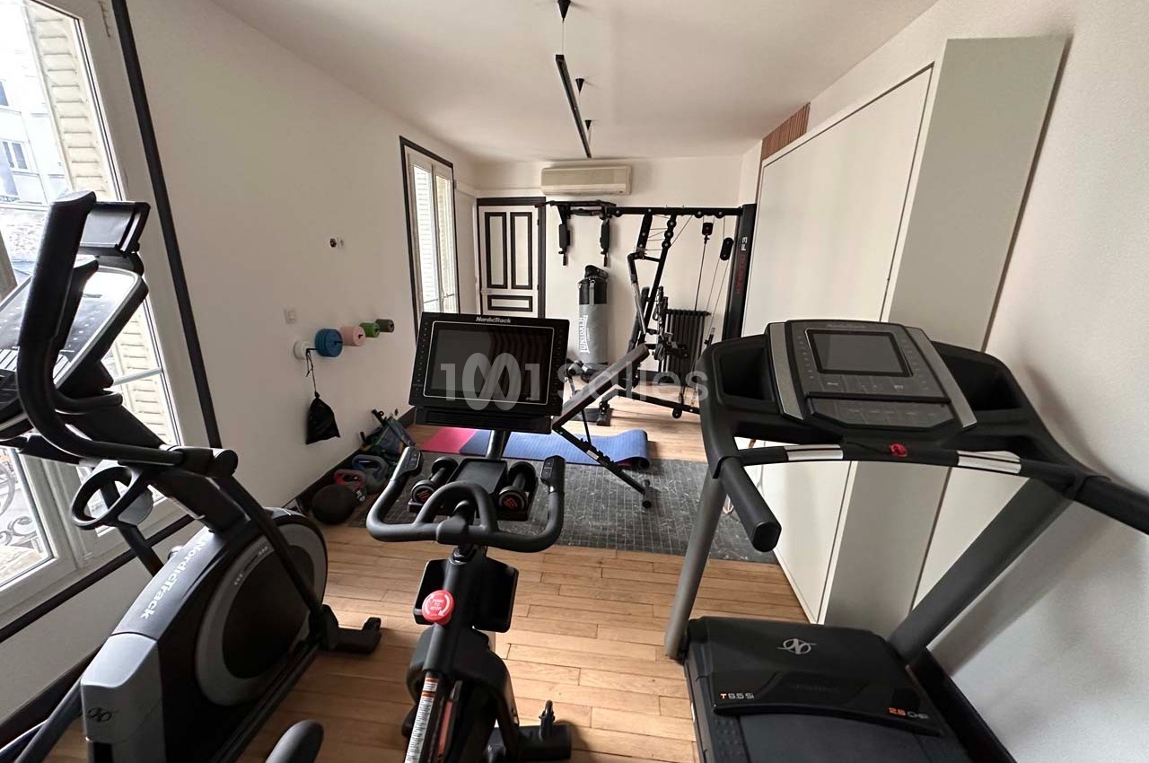 Salle de sport à domicile équipée de vélos d'appartement, tapis de course et matériel de musculation.