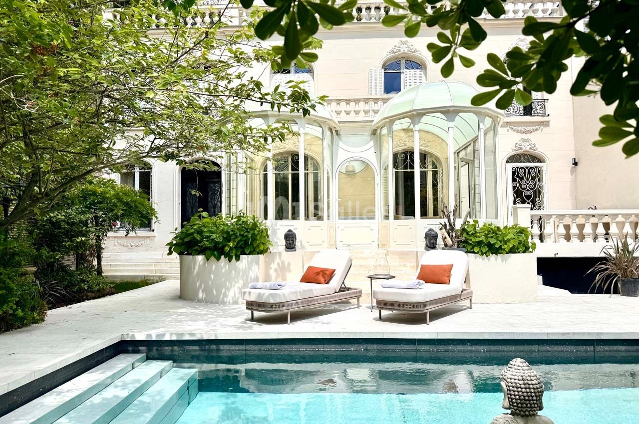Façade d'une maison élégante avec véranda, transats et piscine entourée de verdure.
