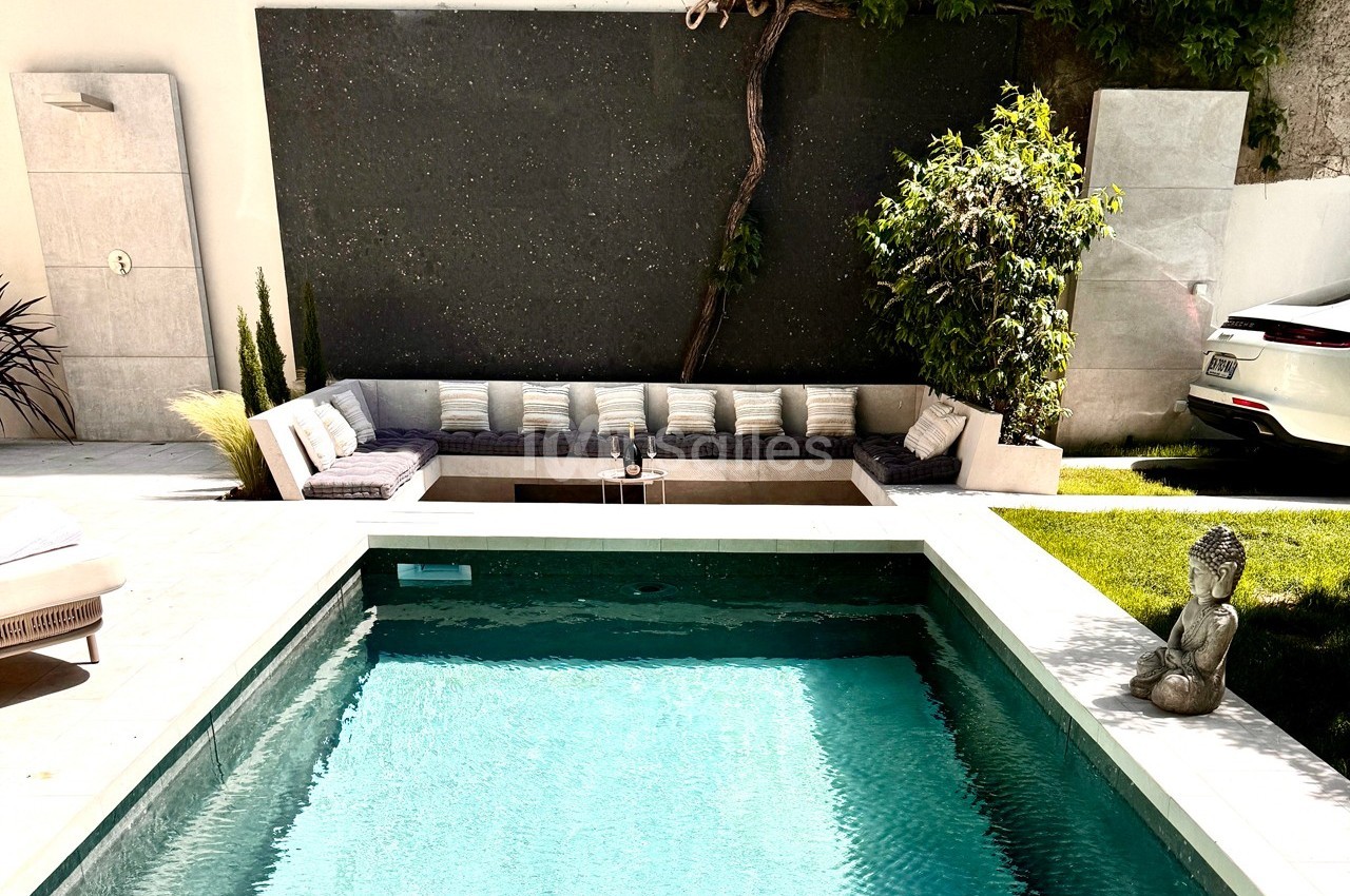 Piscine extérieure entourée de verdure, avec un coin salon moderne et une statue décorative au bord de l'eau.