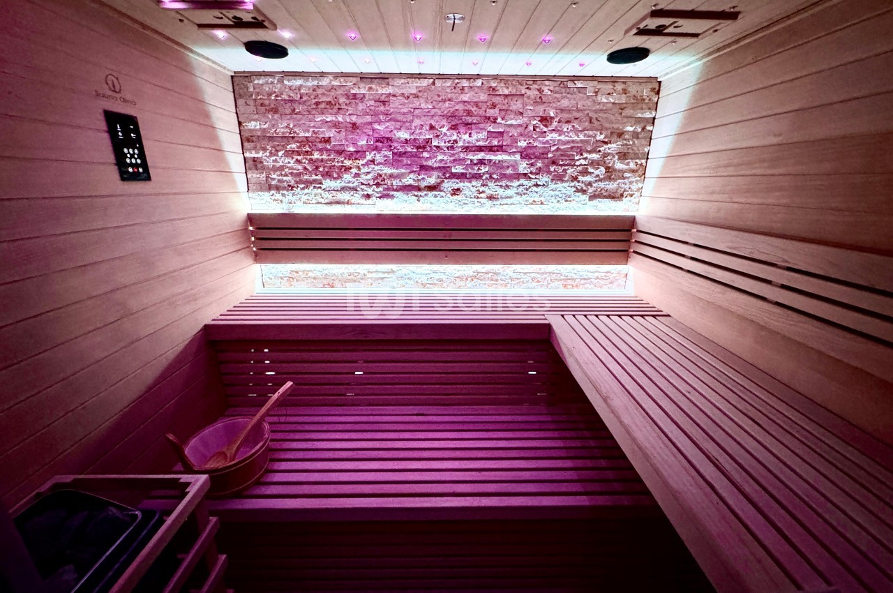 Intérieur d'un sauna en bois avec éclairage tamisé violet et un seau en bois posé au sol.