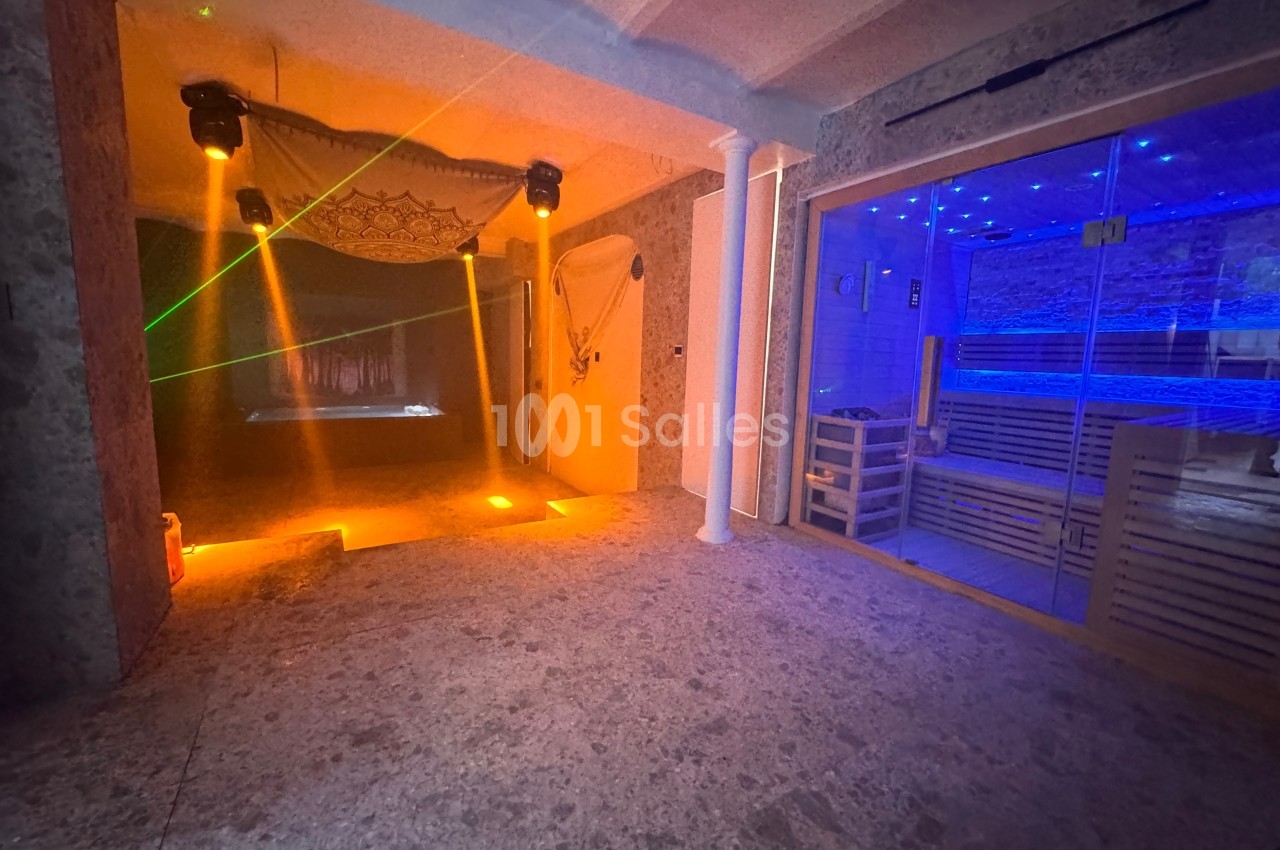 Salle de bien-être avec sauna vitré éclairé en bleu, projecteurs lumineux et ambiance tamisée.