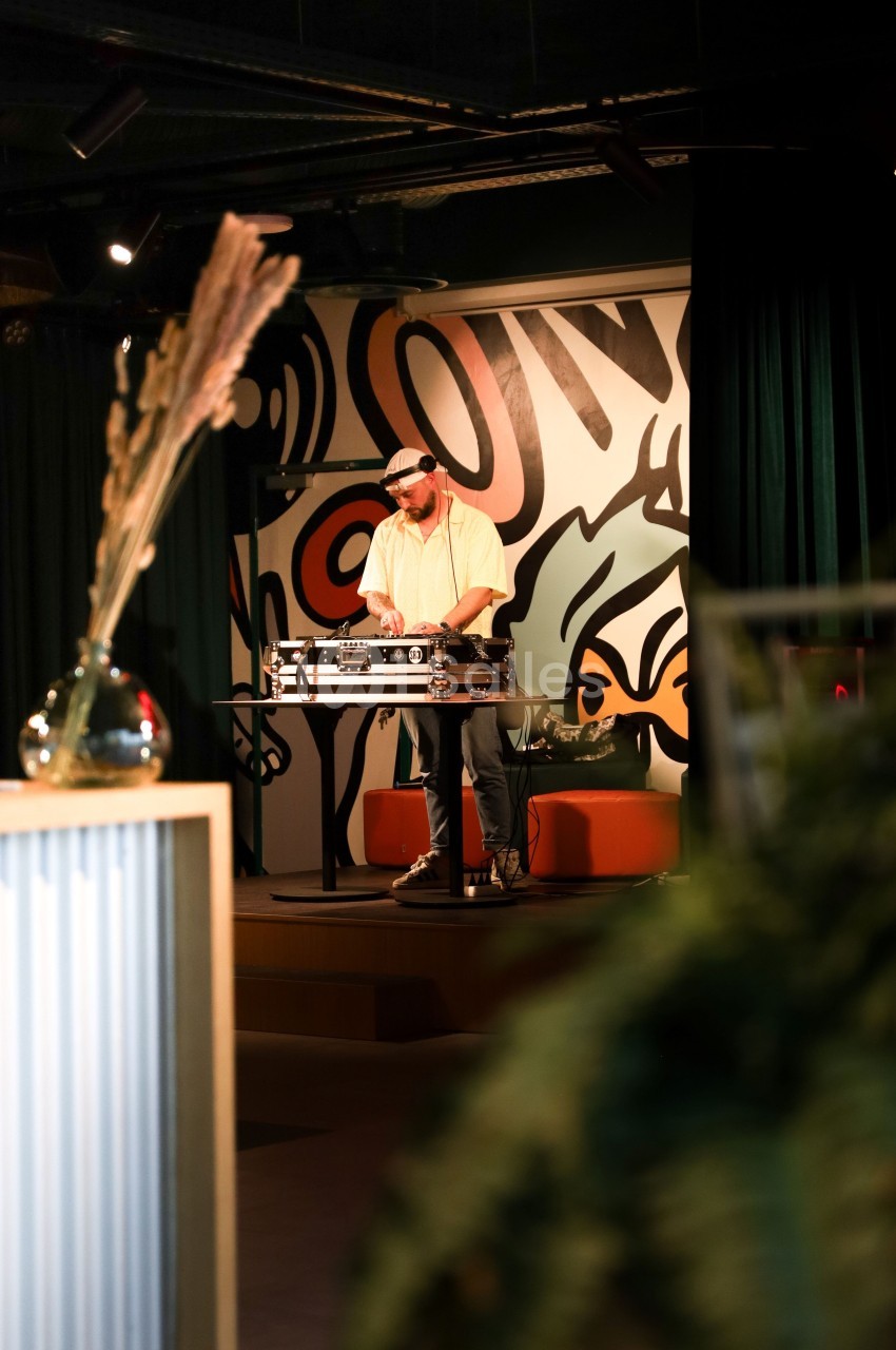 Un DJ mixe sur une table de mixage dans un espace intérieur décoré avec des motifs muraux colorés.