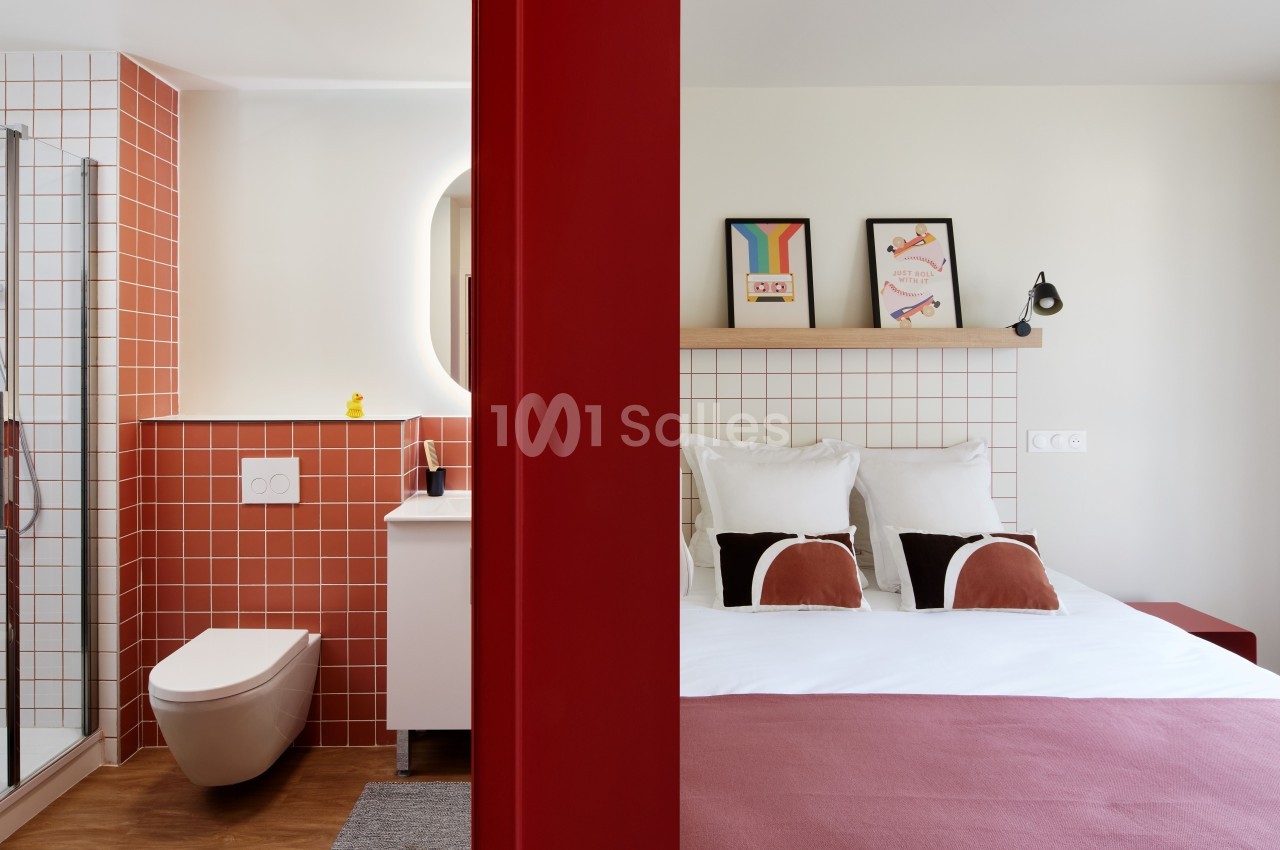 Chambre d'hôtel avec lit double, salle de bain attenante à carreaux rouges et décoration murale colorée.