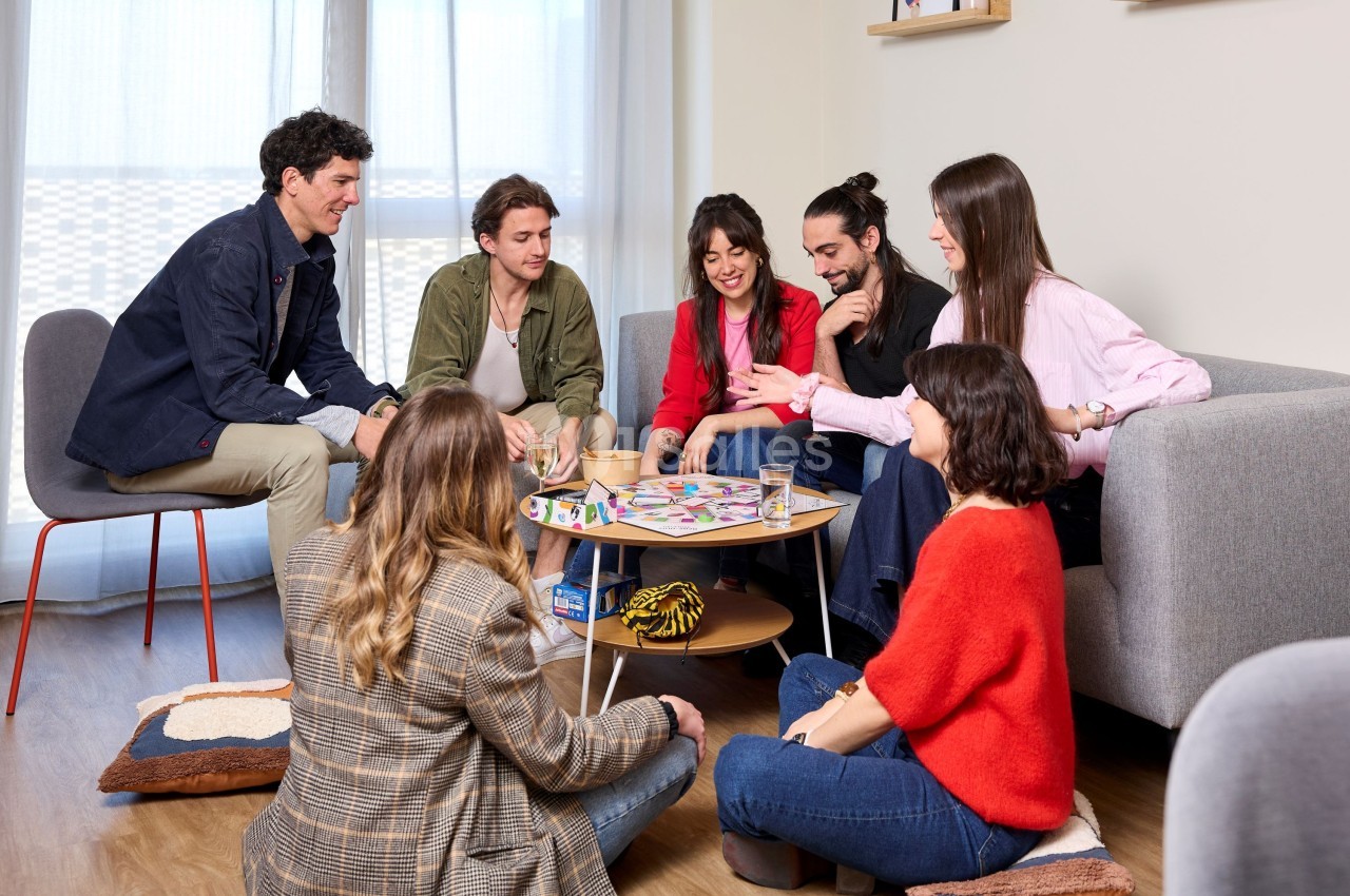 Un groupe de personnes joue à un jeu de société autour d'une table basse dans un salon lumineux.
