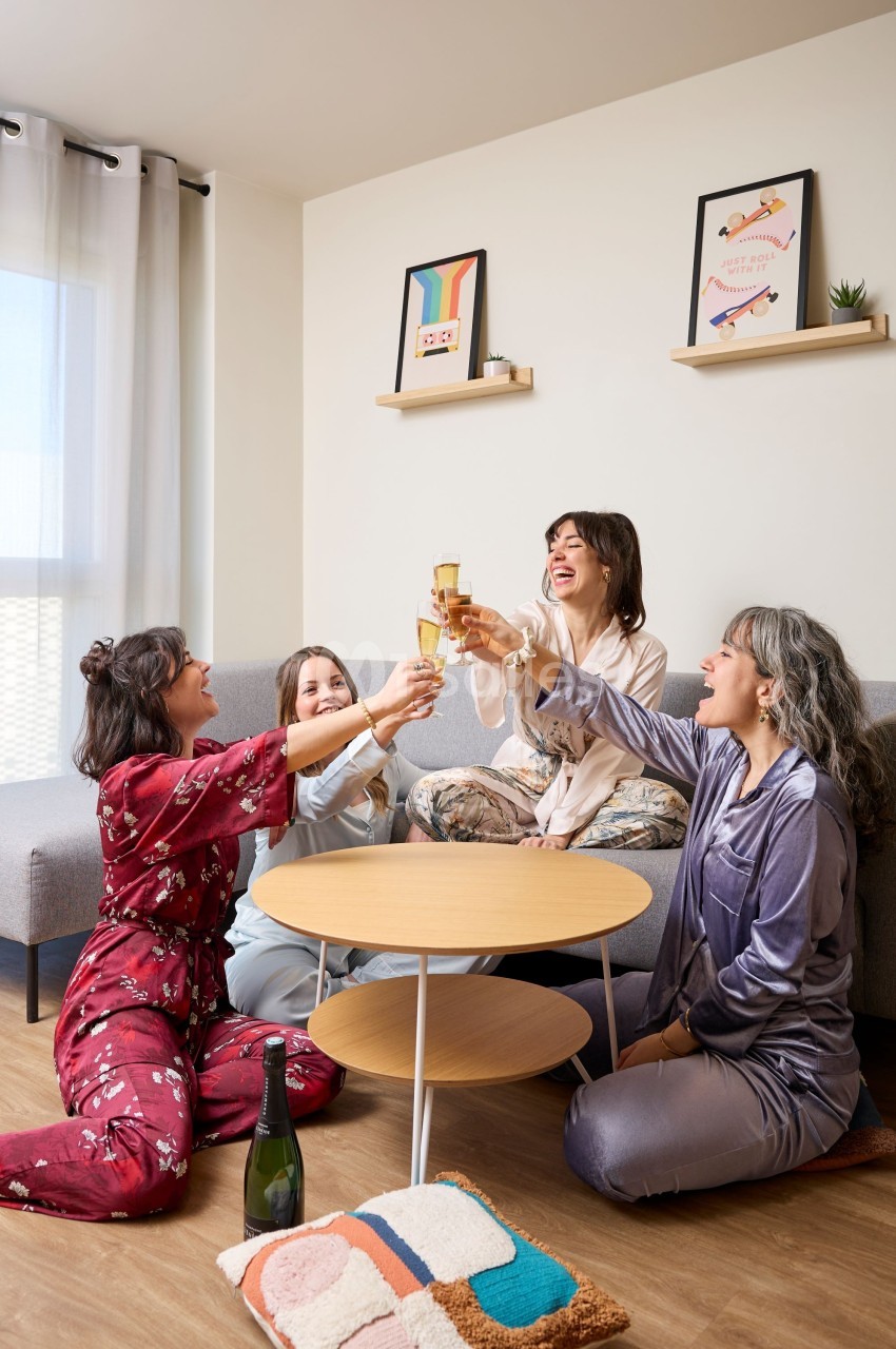 Quatre femmes en pyjama trinquent avec des verres de champagne dans un salon lumineux et convivial.