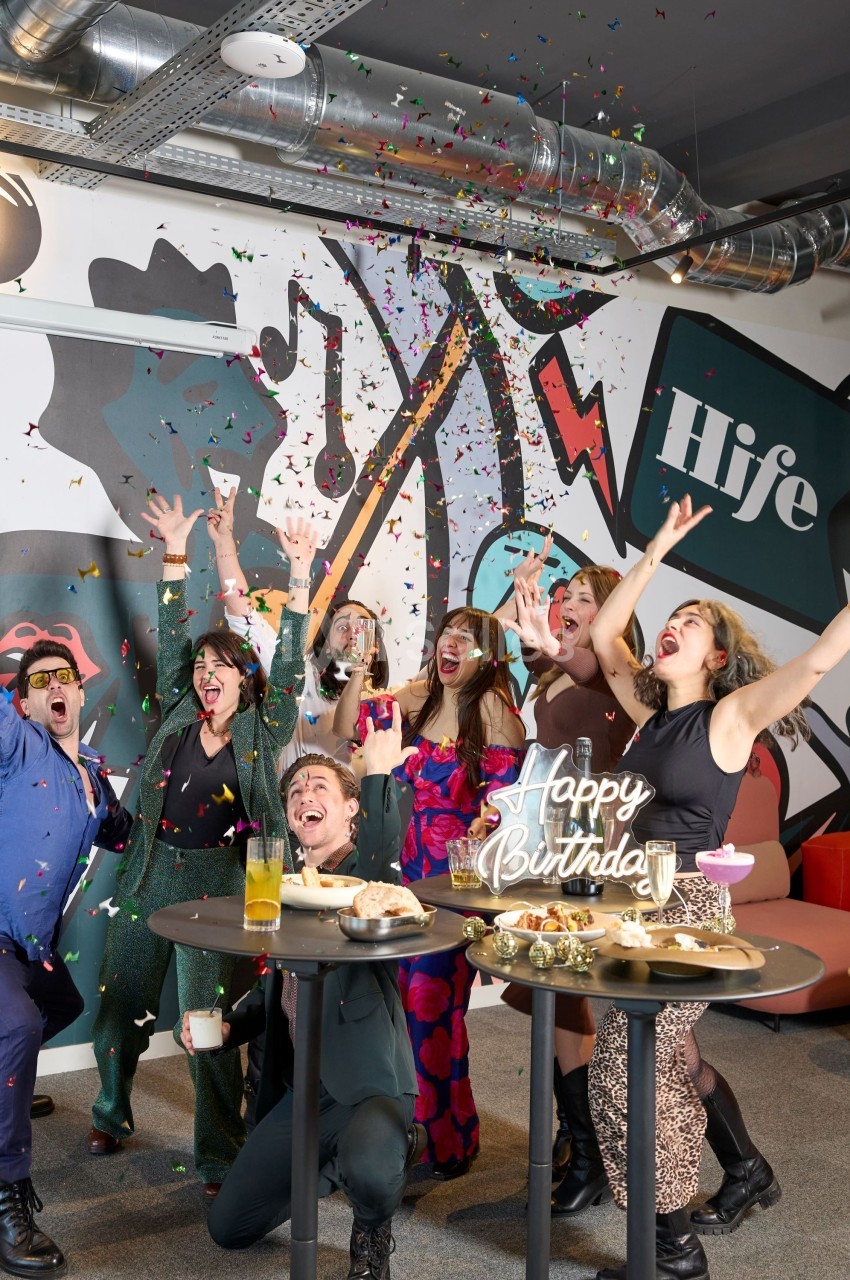 Un groupe de personnes célèbrent un anniversaire avec des confettis, des boissons et un gâteau dans une ambiance festive.