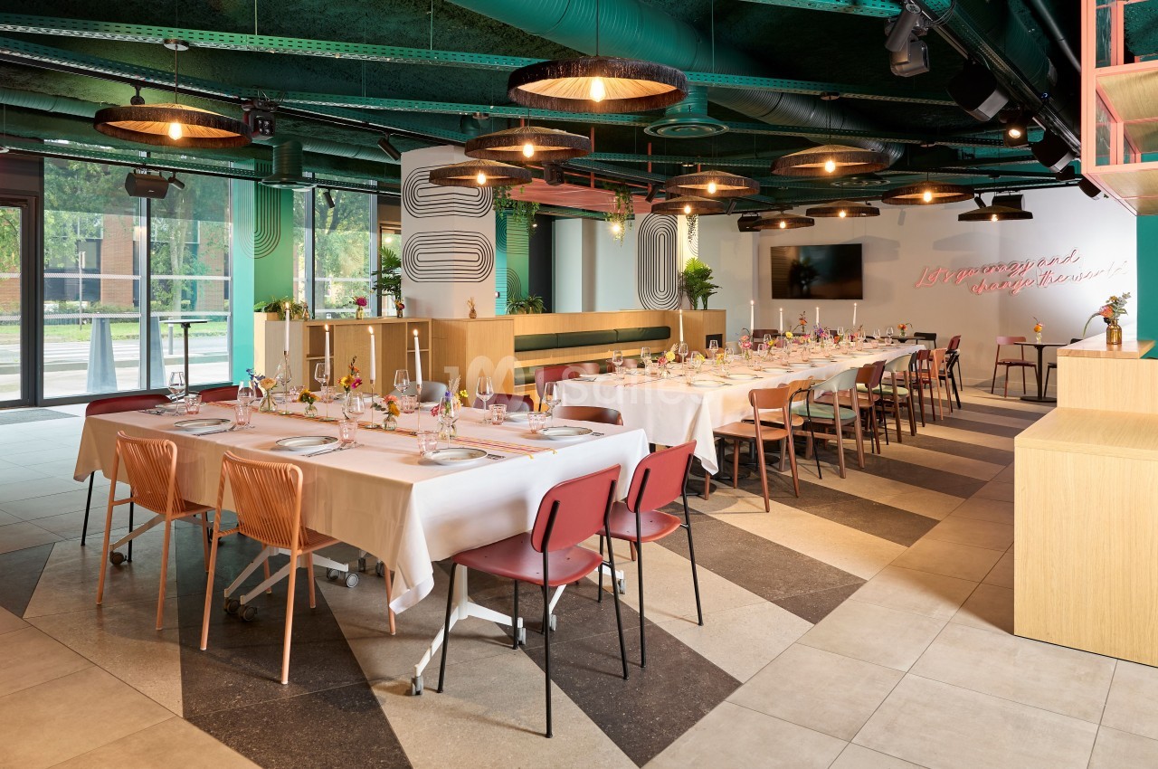 Salle de restaurant moderne avec tables dressées, chaises colorées et décoration lumineuse, vue sur l'extérieur.