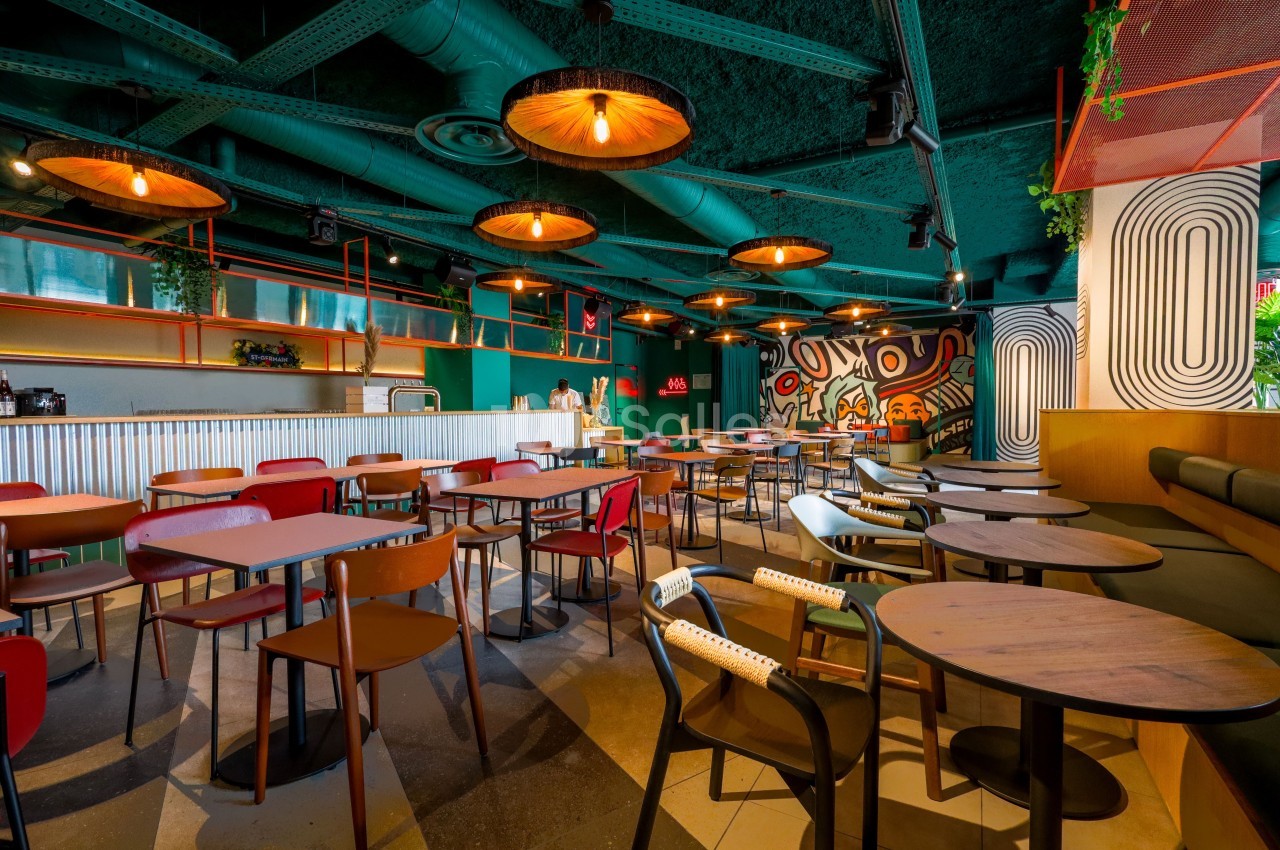 Salle de restaurant moderne avec des tables en bois, des chaises colorées et un éclairage suspendu chaleureux.