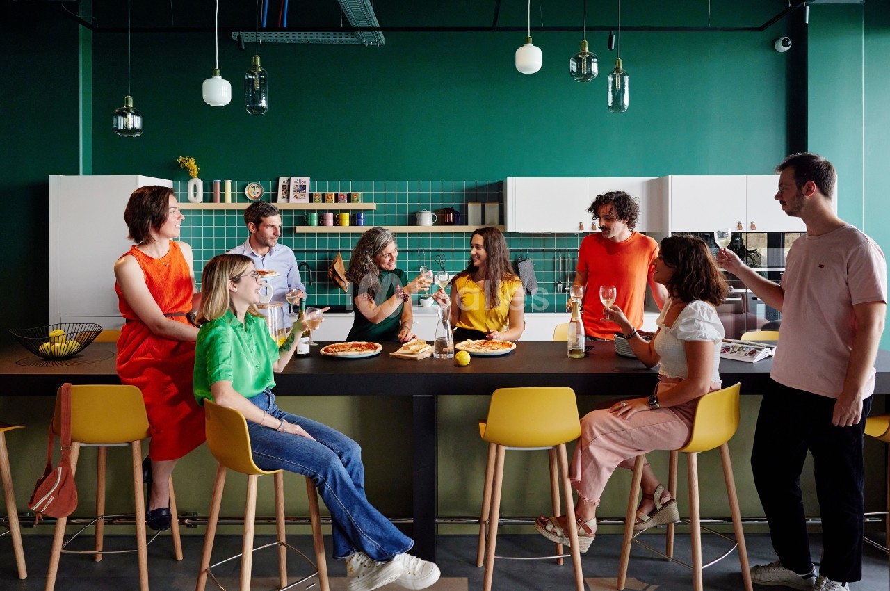Un groupe de personnes assises et debout autour d'un comptoir dans une cuisine moderne, partageant un repas.