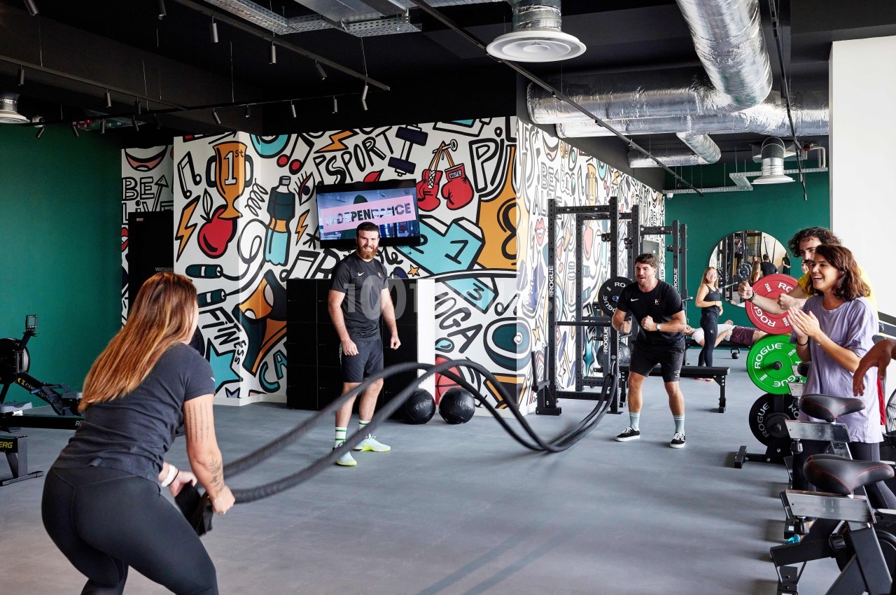 Des personnes s'entraînent dans une salle de sport moderne avec des cordes ondulatoires, sous le regard d'un coach.