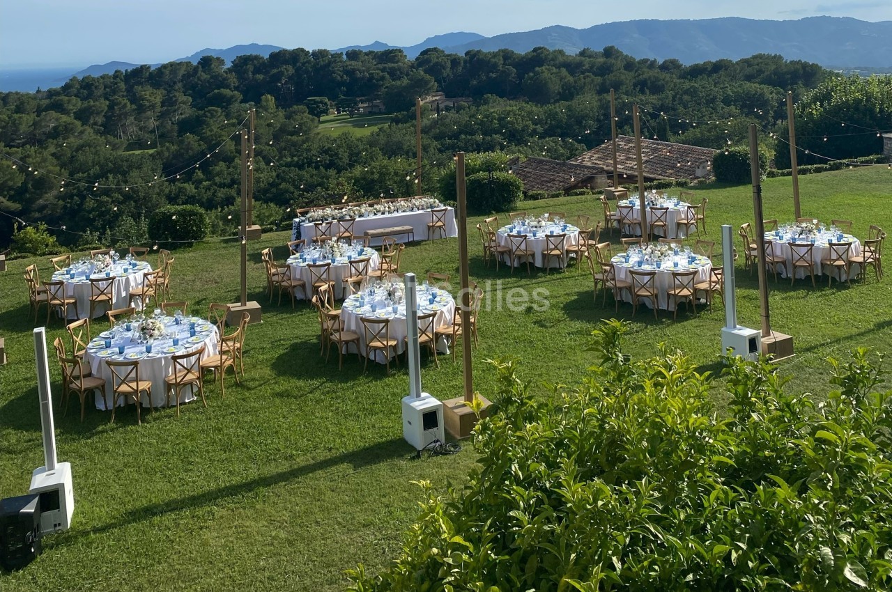Tables rondes dressées pour un événement en plein air sur une pelouse, avec vue sur des collines verdoyantes.