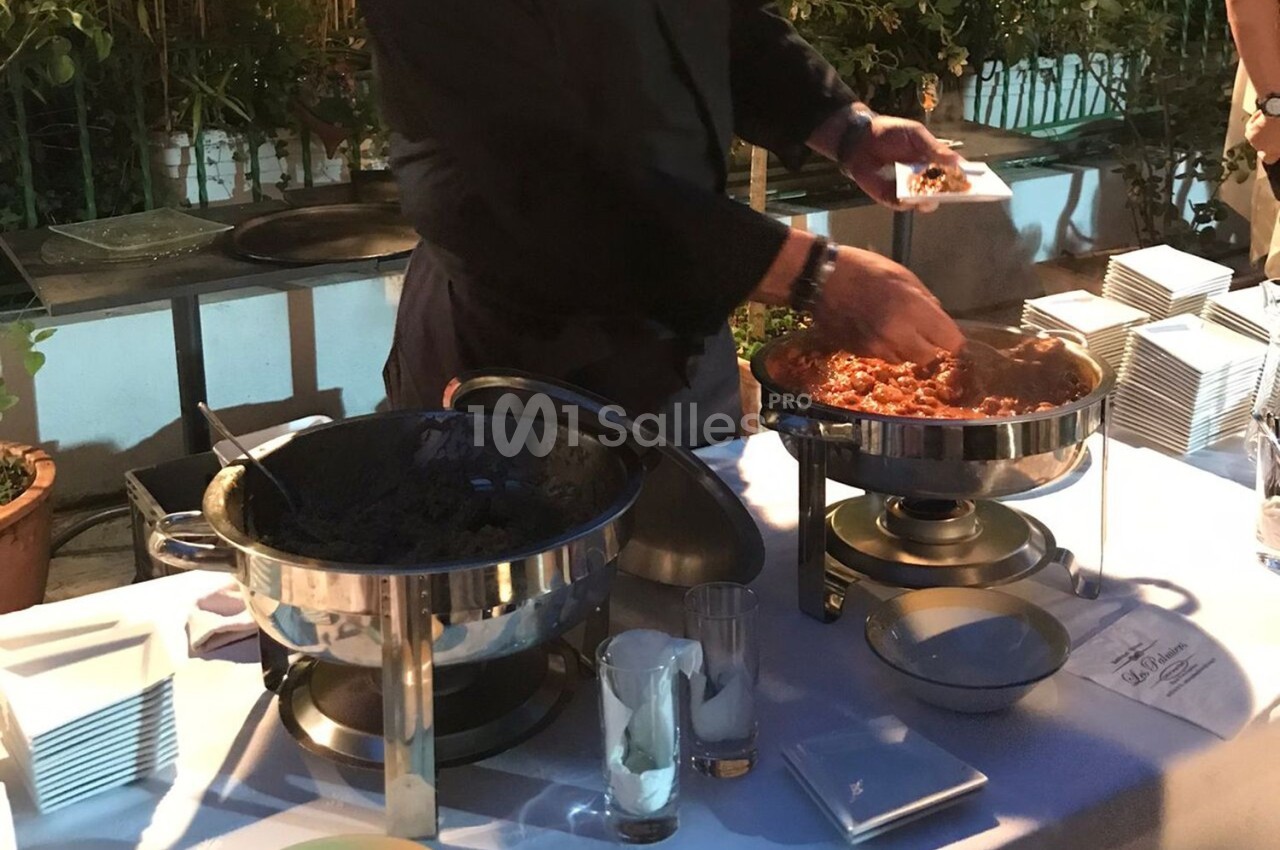 Un serveur remplit une assiette avec un plat chaud présenté dans un chafing dish lors d'un buffet en extérieur.