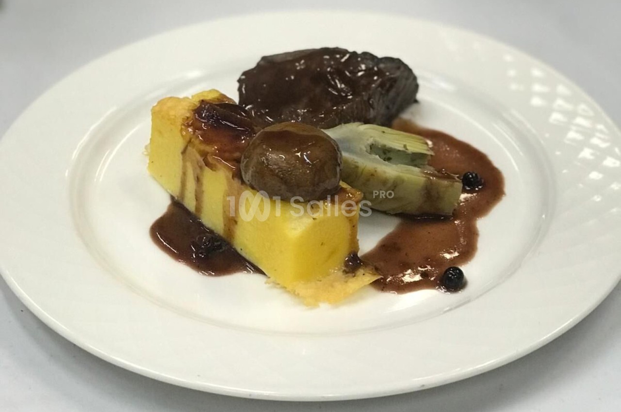 Assiette de polenta, artichaut, champignon et viande nappés de sauce brune, servie sur une table blanche.
