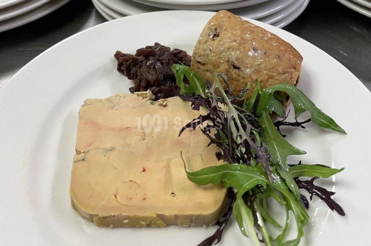 Assiette avec tranche de foie gras, confit d'oignons, pain aux céréales et salade verte sur un fond de table dressée.