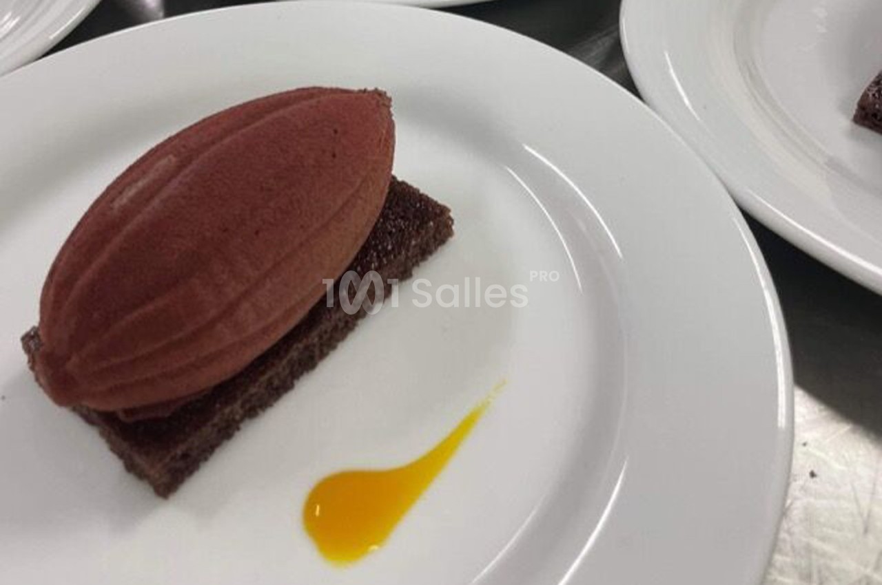 Une quenelle de sorbet rouge sur un biscuit au chocolat, accompagnée d'une goutte de coulis jaune.