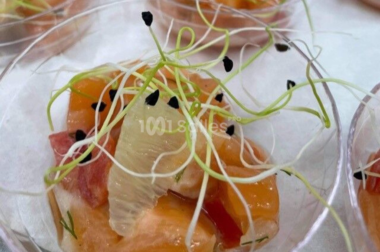Dés de saumon et agrumes garnis de graines noires et pousses vertes, présentés dans une verrine transparente.