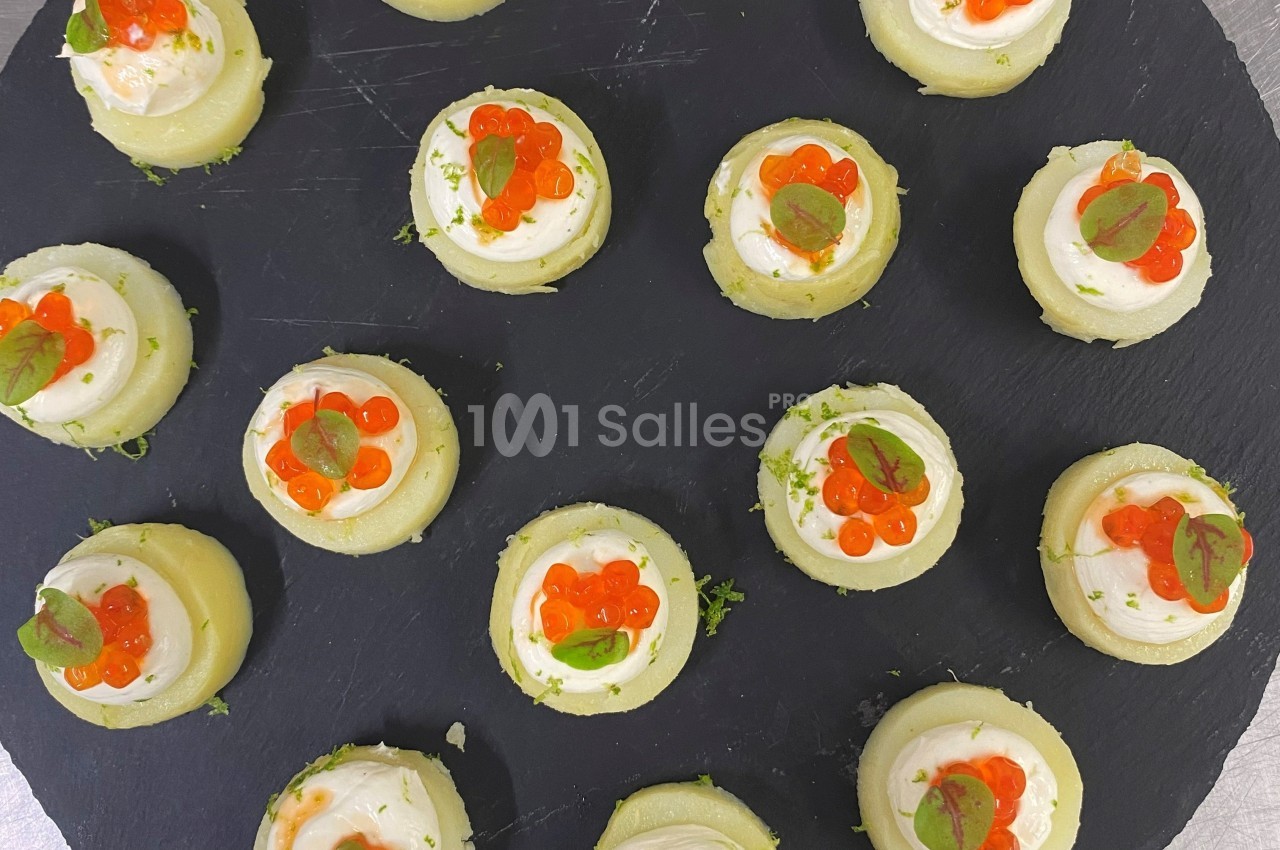 Assortiment de bouchées apéritives sur ardoise, garnies de crème, œufs de poisson et feuilles vertes.