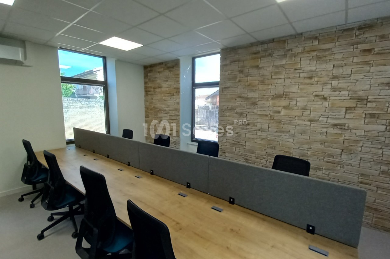 Salle de réunion avec une grande table en bois, chaises noires, cloison centrale et mur en pierre apparente.