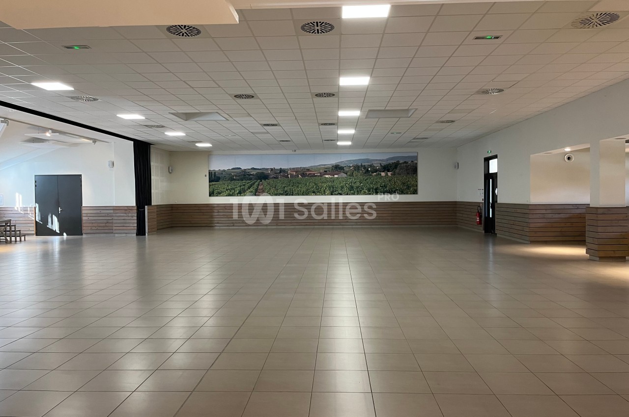 Salle spacieuse avec carrelage clair, plafond à dalles blanches et fresque murale représentant un paysage rural.