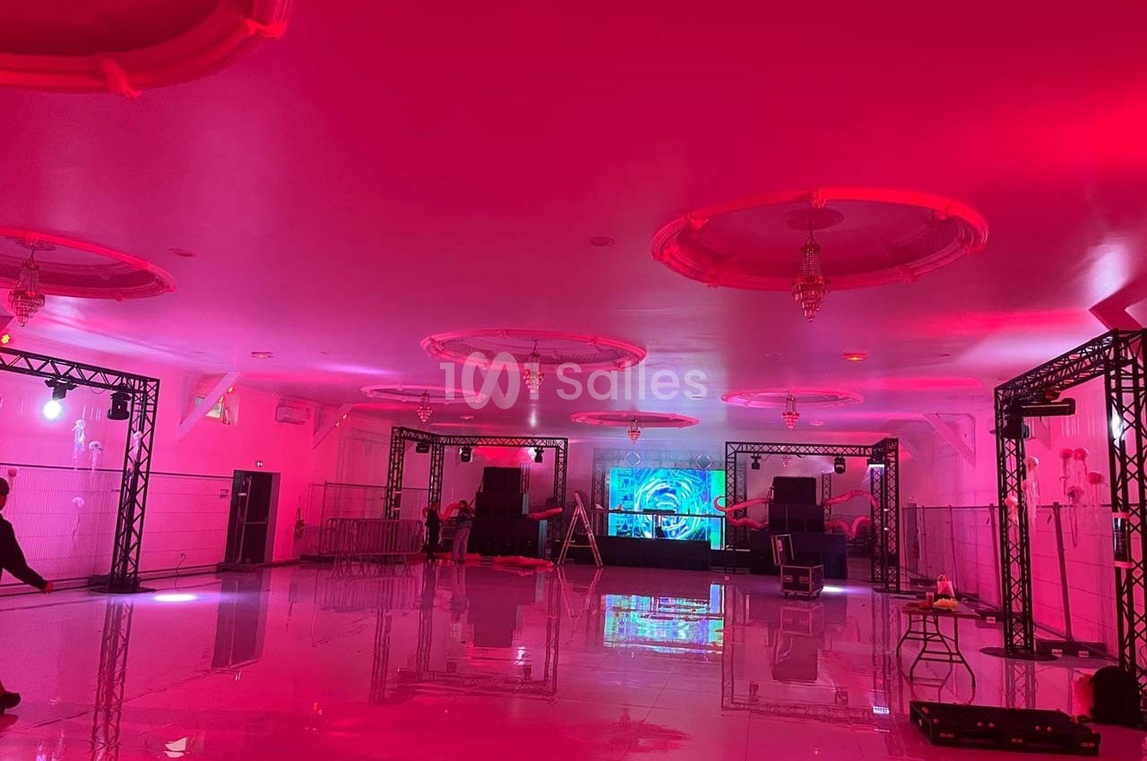 Salle de réception vide éclairée par des lumières roses, avec une scène équipée de matériel audio et visuel.