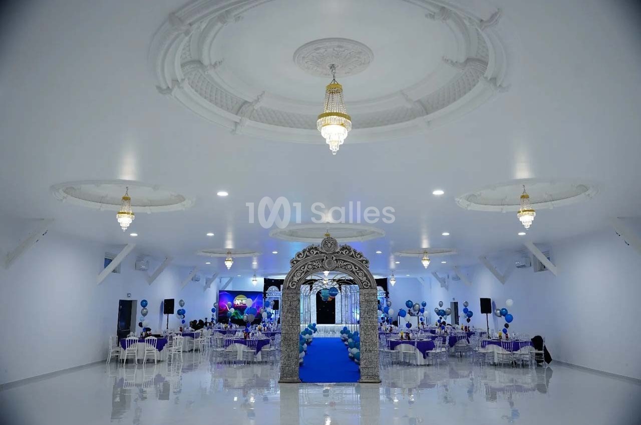 Salle de réception décorée avec des tables dressées, des ballons bleus et une arche ornée au centre.