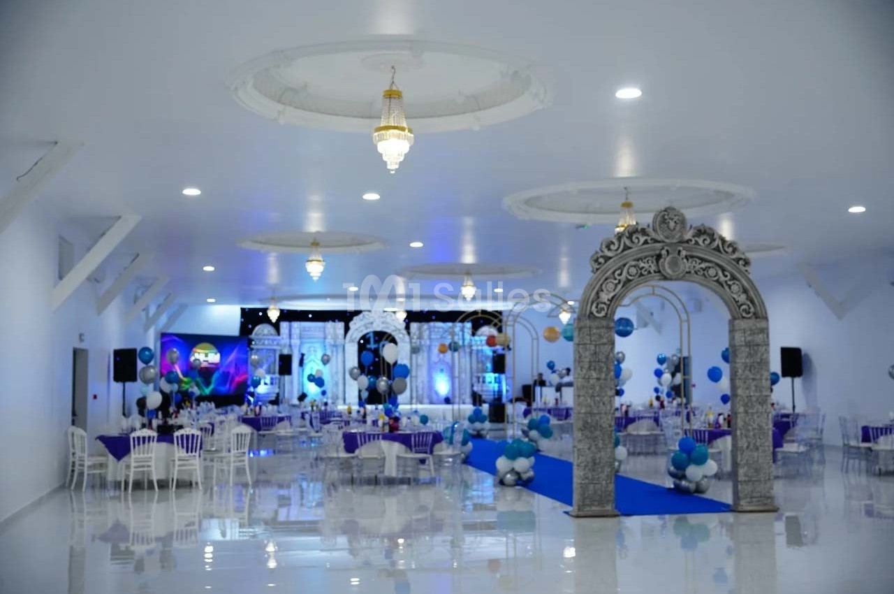 Salle de réception décorée avec des arches, des ballons bleus et blancs, et des tables dressées pour un événement.