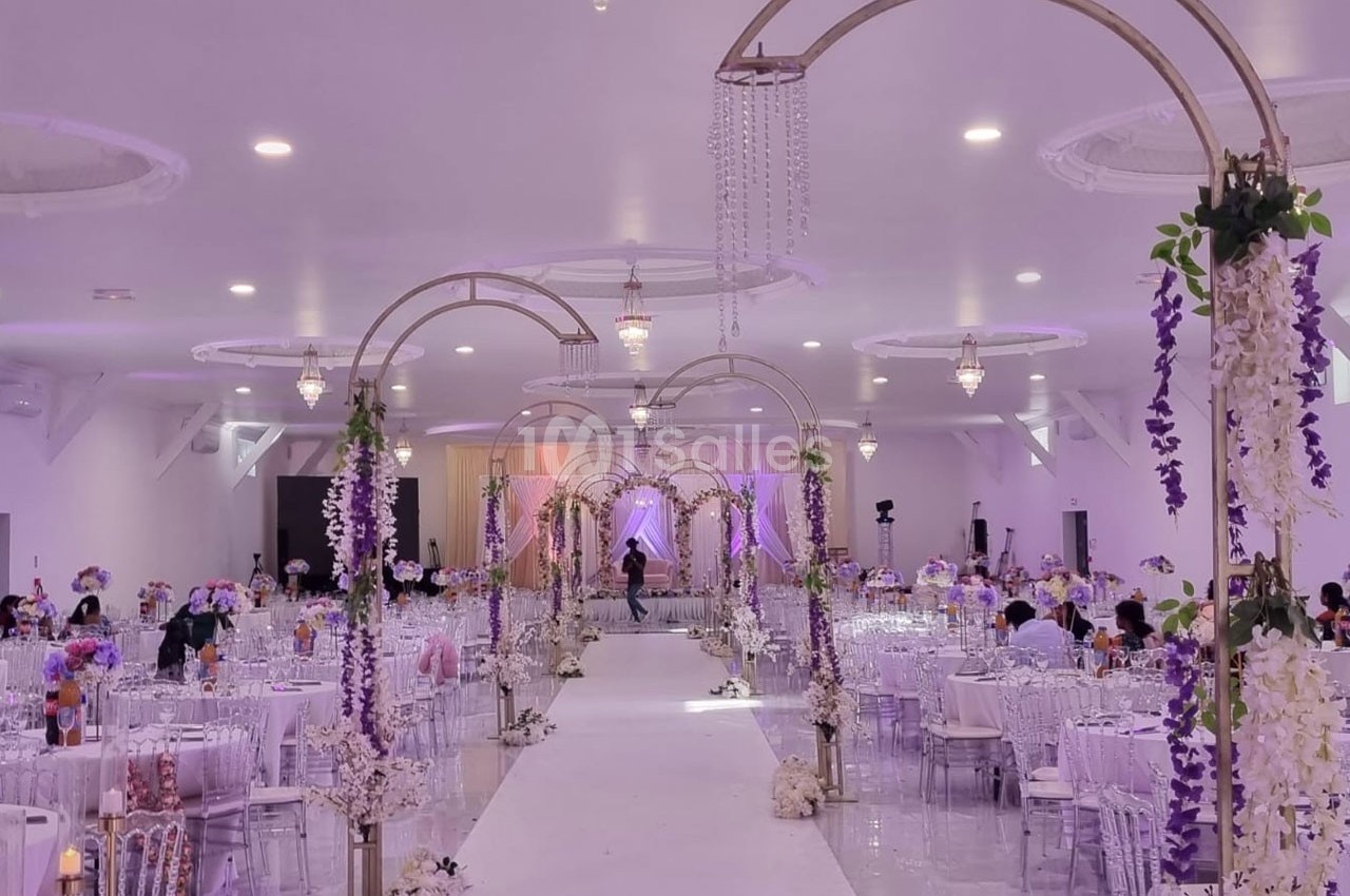 Salle de réception décorée avec des arches fleuries, des tables dressées et un éclairage doux dans des tons violets.